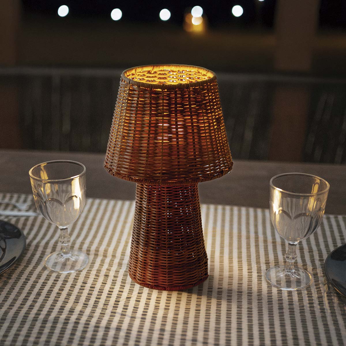 Lampe allumée sur une nappe rayée entre deux verres, table dressée en terrasse