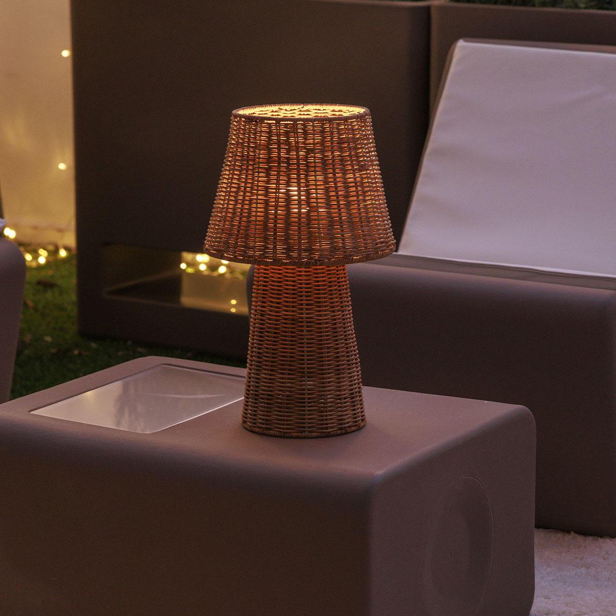 Vue de face de la lampe posée sur un cube, ambiance salon d'extérieur le soir
