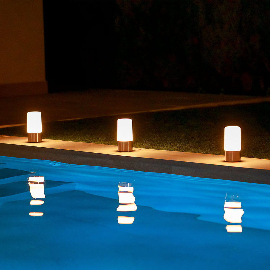 Trois lampes alignées au bord d'une piscine, lumière chaude et reflets sur l'eau.