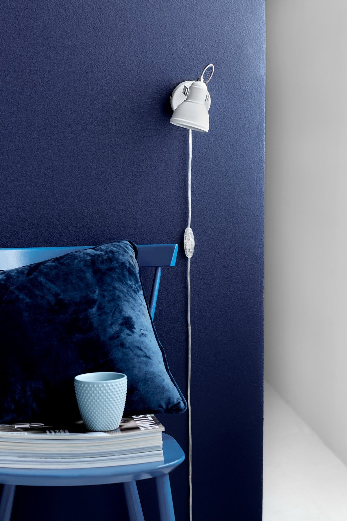Applique blanche fixée sur mur bleu, cordon avec interrupteur pendant le long du mur.