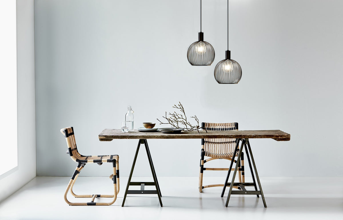 Deux suspensions noires suspendues au-dessus d'une table en bois avec chaises
