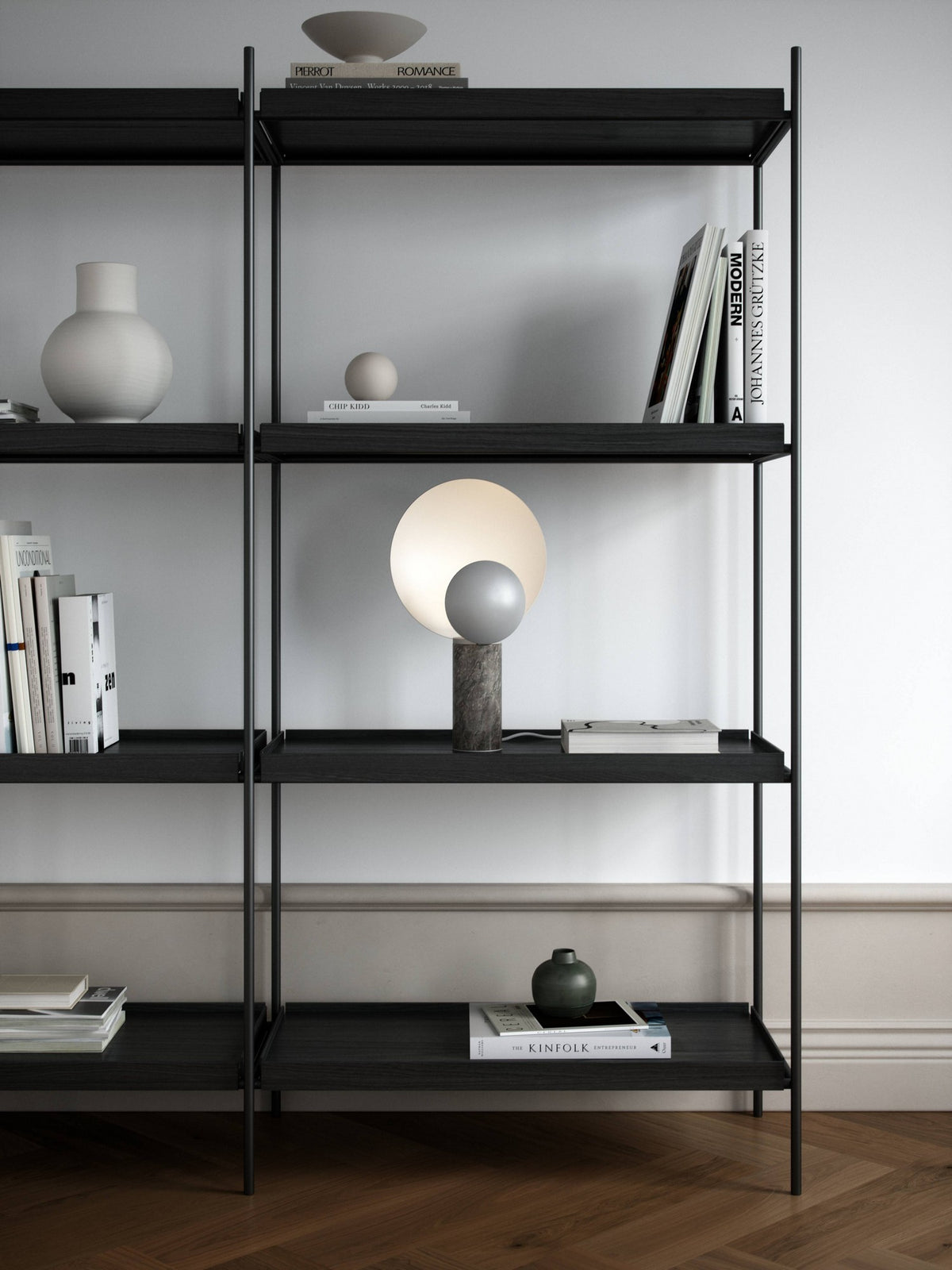 Mise en ambiance, lampe posée sur une étagère noire parmi livres et objets décoratifs.