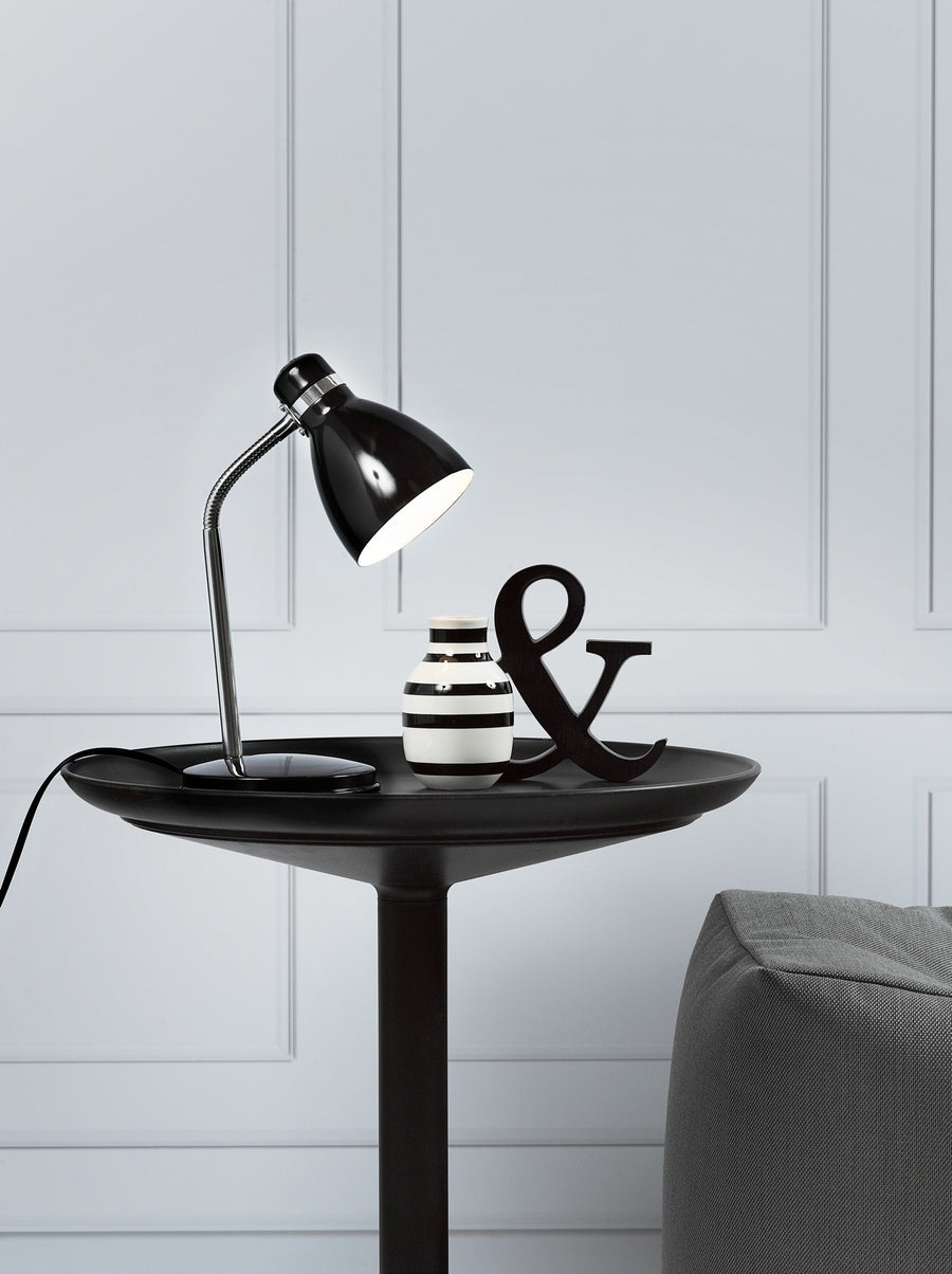 Lampe noire posée sur table noire, vase rayé et lettre & en déco.