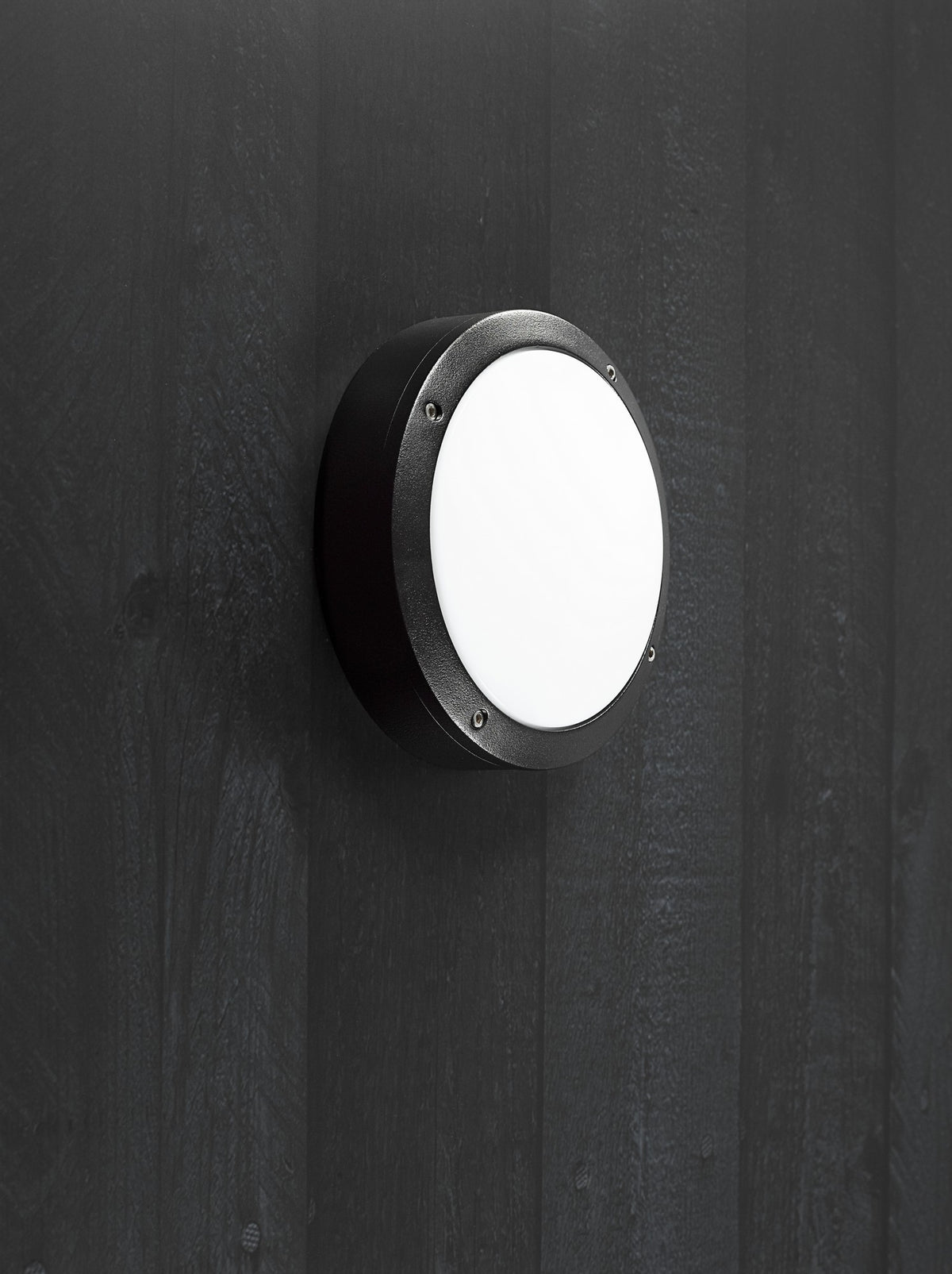 Luminaire extérieur noir installé sur une paroi sombre, lumière allumée