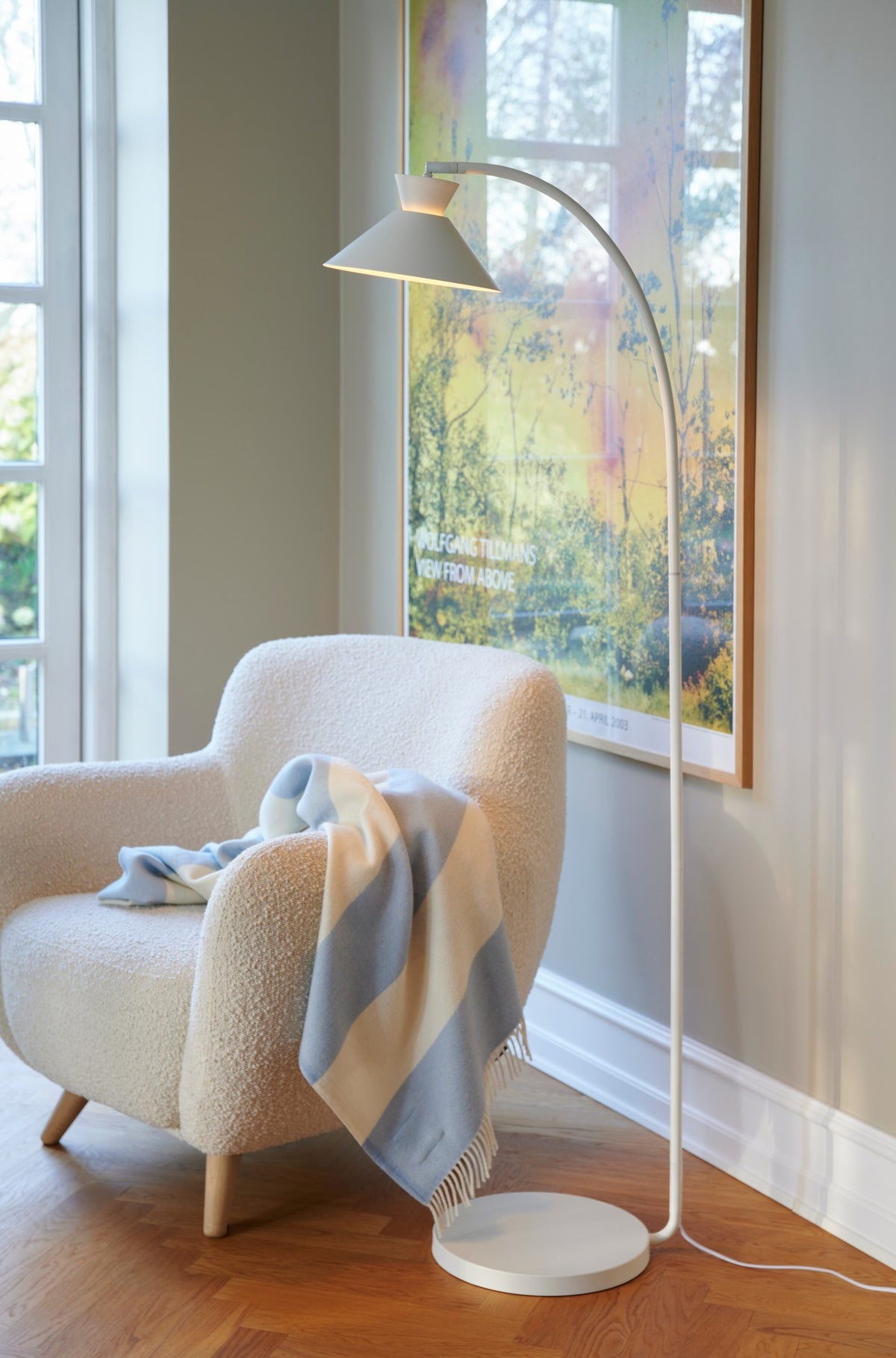 Mise en ambiance salon, fauteuil bouclé et lampadaire blanc près d'une fenêtre