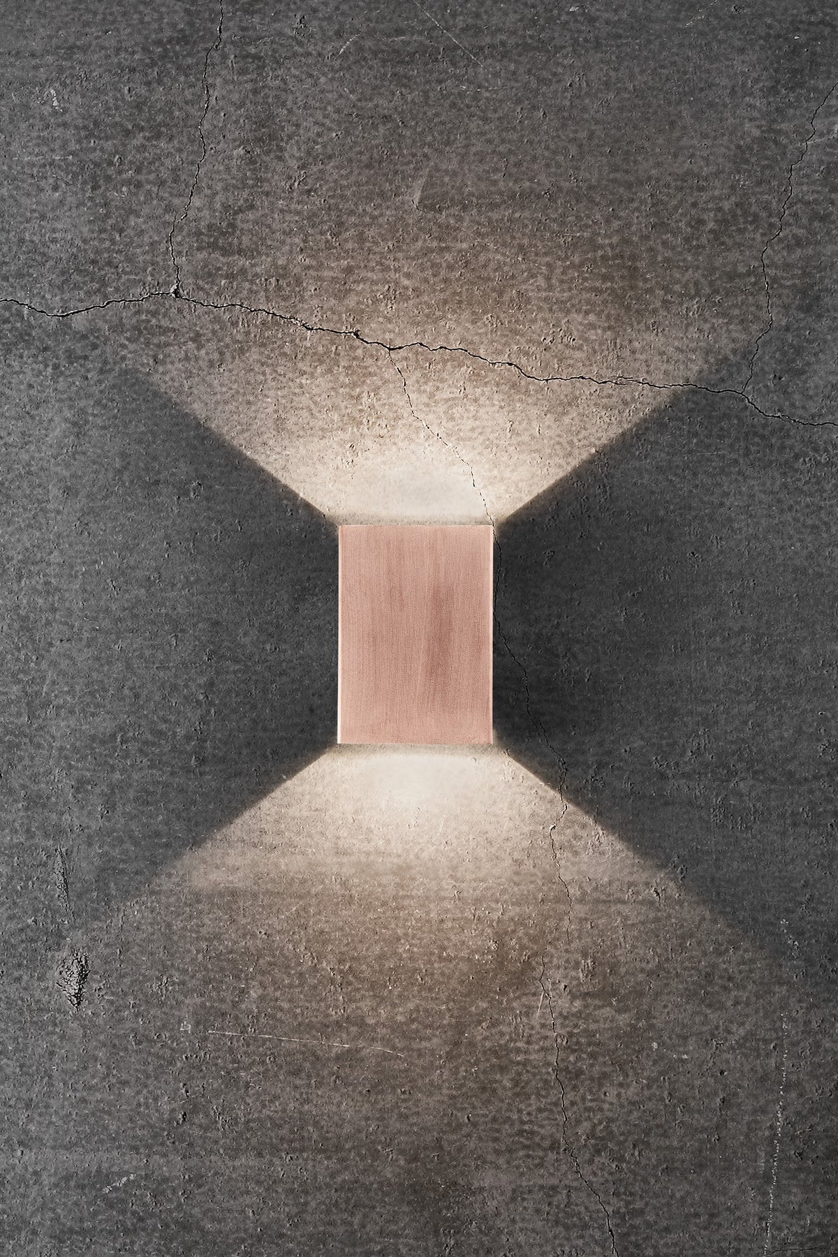 Mise en ambiance : applique murale cuivrée éclairant un mur de béton en haut et en bas.