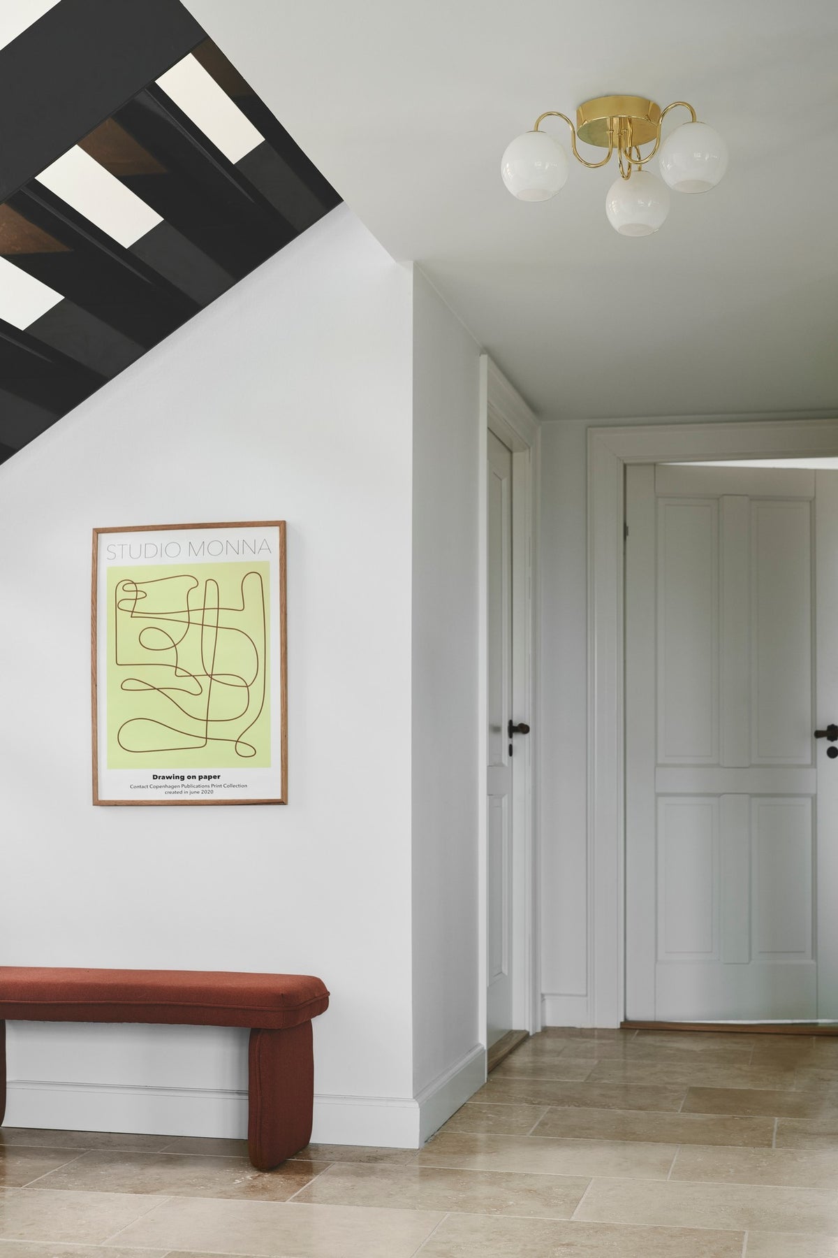 Plafonnier doré à trois globes installé au plafond d'un couloir blanc lumineux.