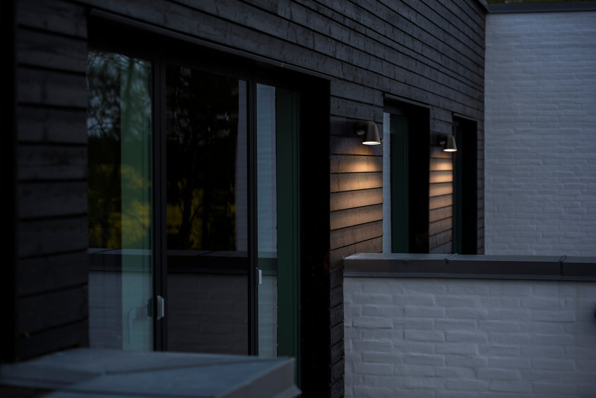 Mise en ambiance nocturne de deux appliques noires sur un bardage bois.