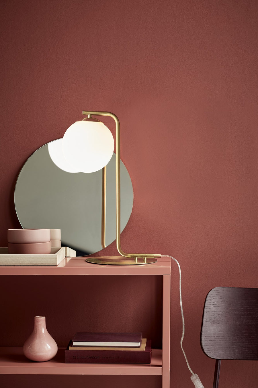 Lampe allumée posée sur une console rose devant un miroir rond