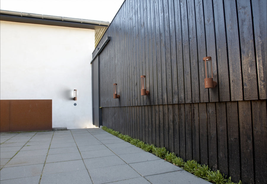 Plusieurs appliques en corten installées sur une façade sombre en extérieur.
