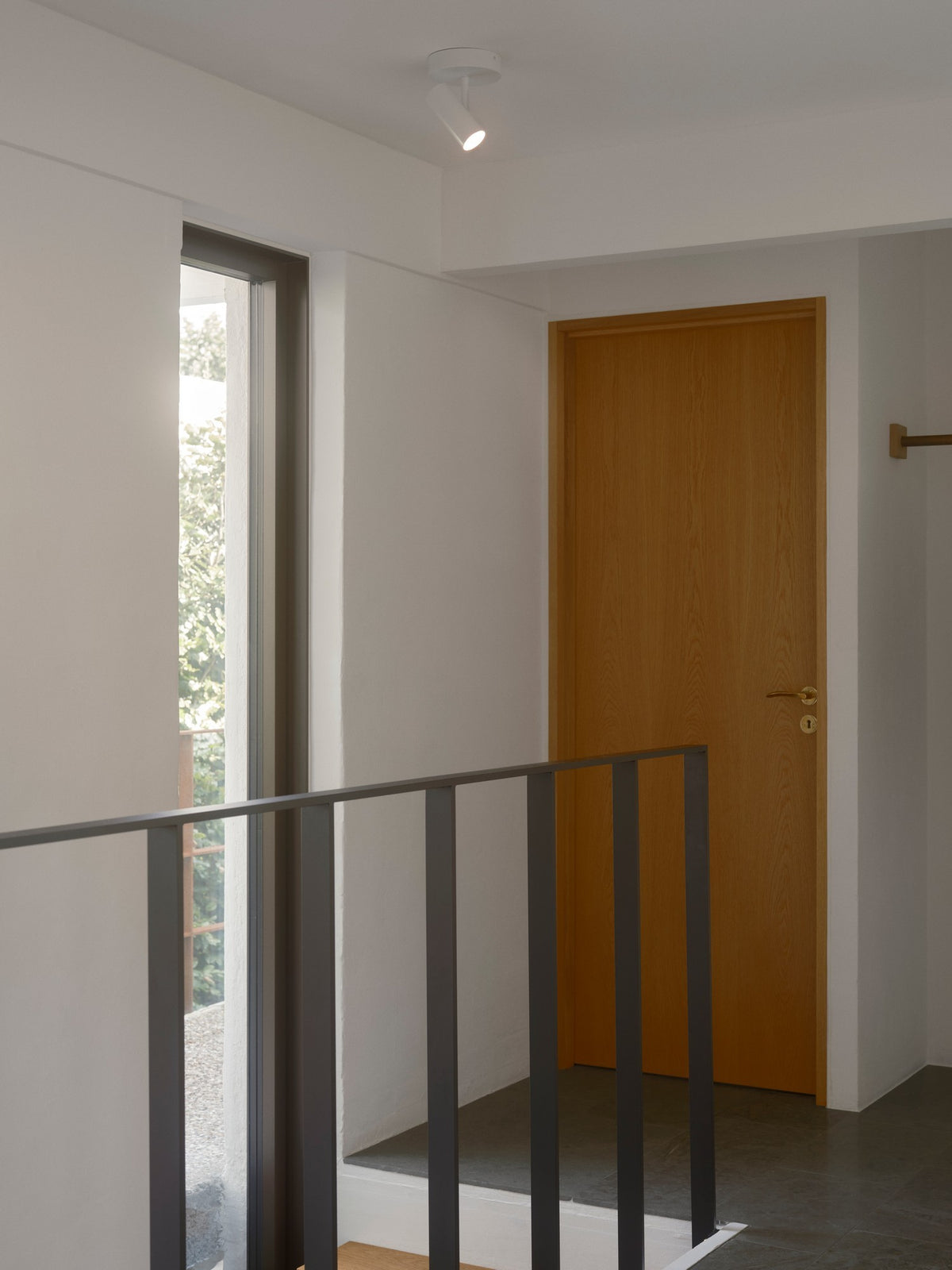Mise en ambiance dans un couloir : petit plafonnier blanc éclairant une porte en bois.
