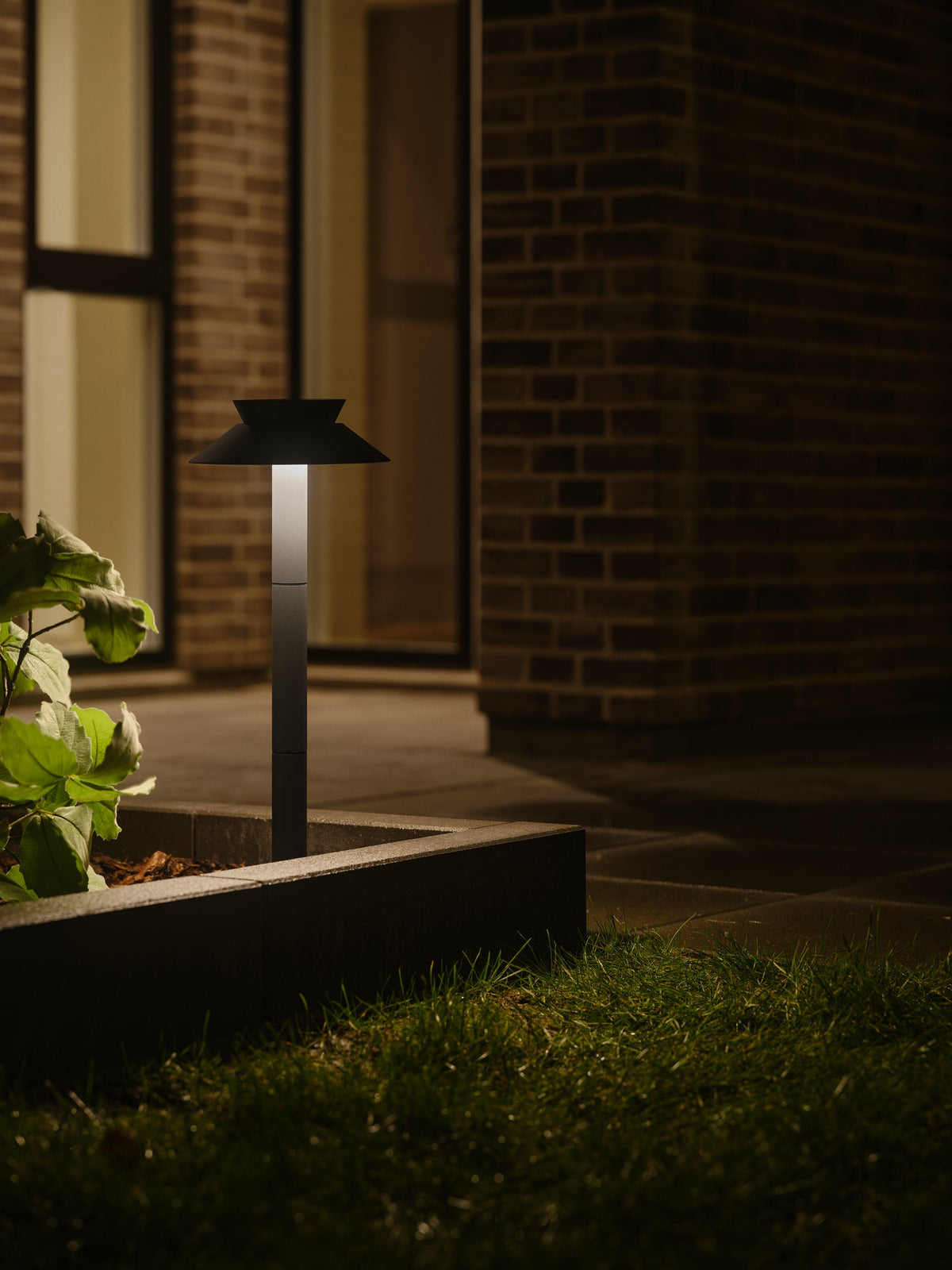 Mise en ambiance nocturne, borne allumée près d'une jardinière en pierre et d'un mur