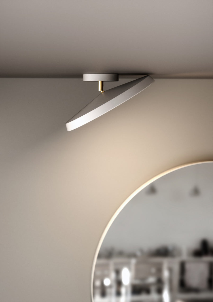 Détail de la finition avec tige dorée et abat-jour blanc incliné sous le plafond.