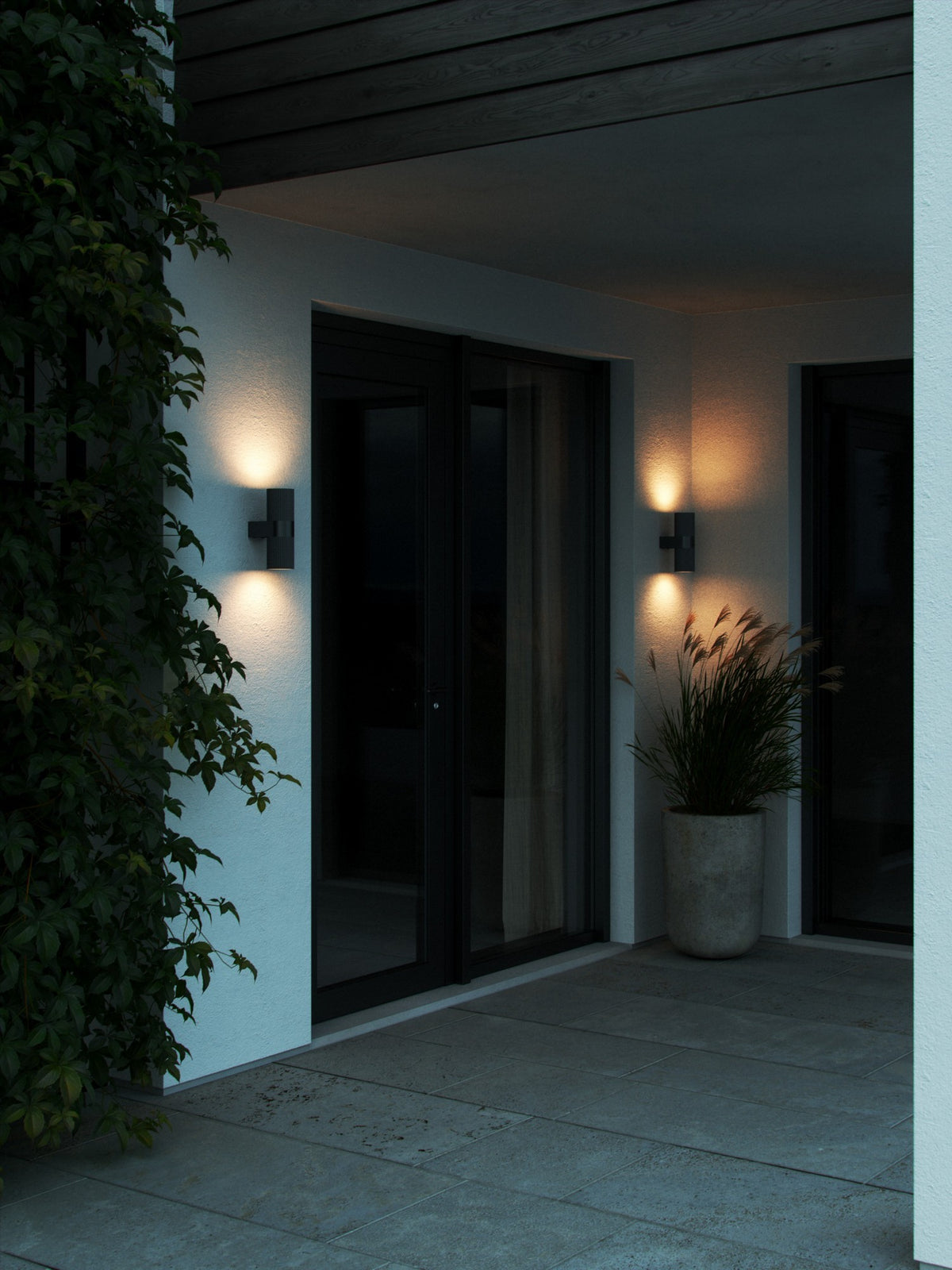 Mise en ambiance nocturne de deux appliques murales noires éclairant une façade extérieure