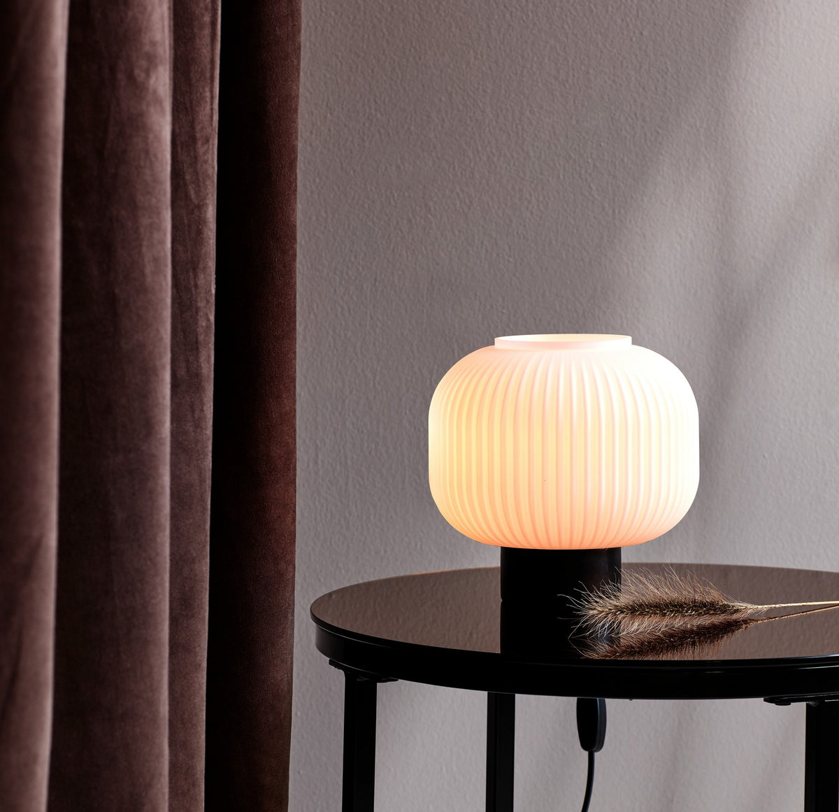 Mise en ambiance sur une table ronde noire, lampe allumée près d'un rideau marron