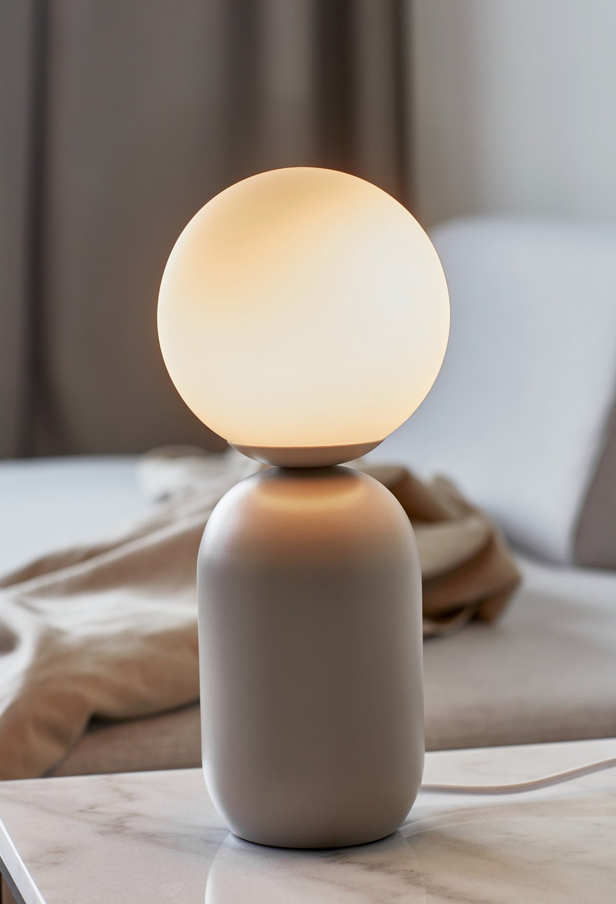Mise en ambiance : lampe allumée sur une table de nuit en marbre, près d'un lit.