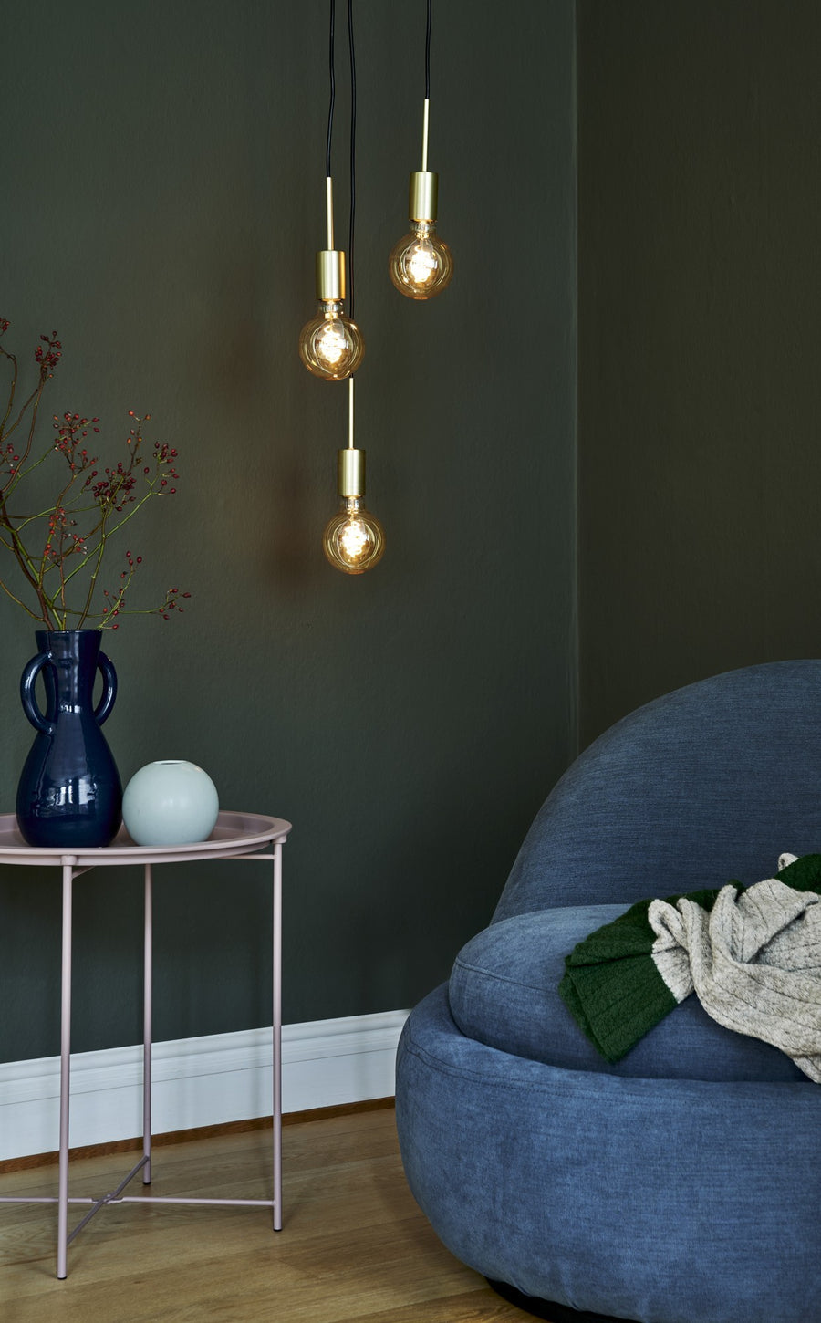 Suspension dorée allumée au-dessus d'une table rose et fauteuil bleu nuit