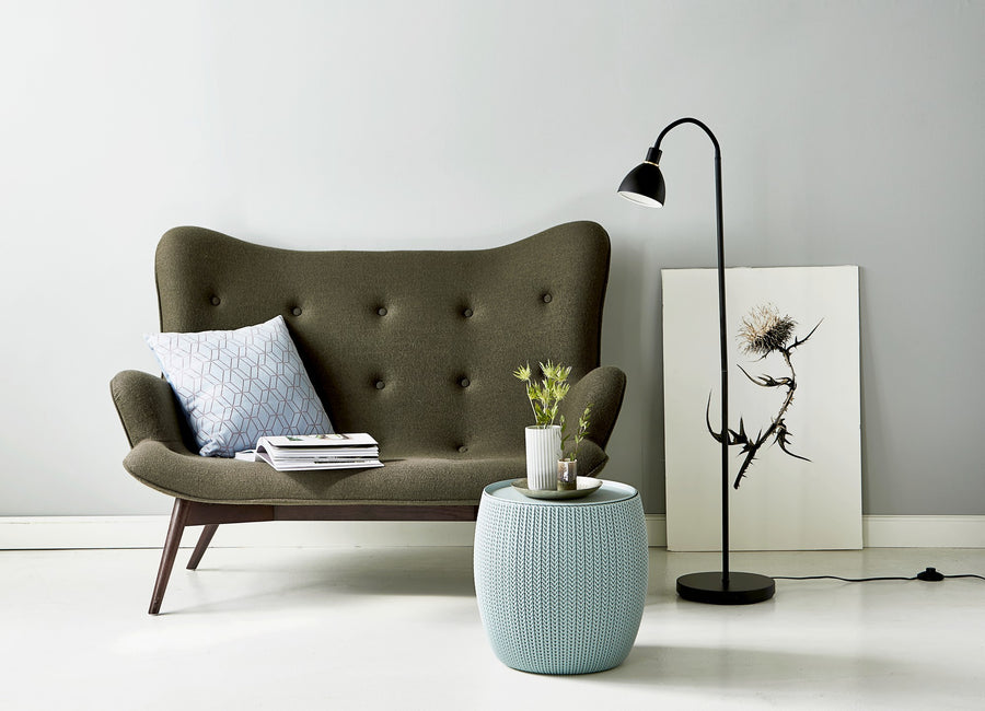 Lampadaire noir allumé près d'un canapé gris et d'un pouf bleu.