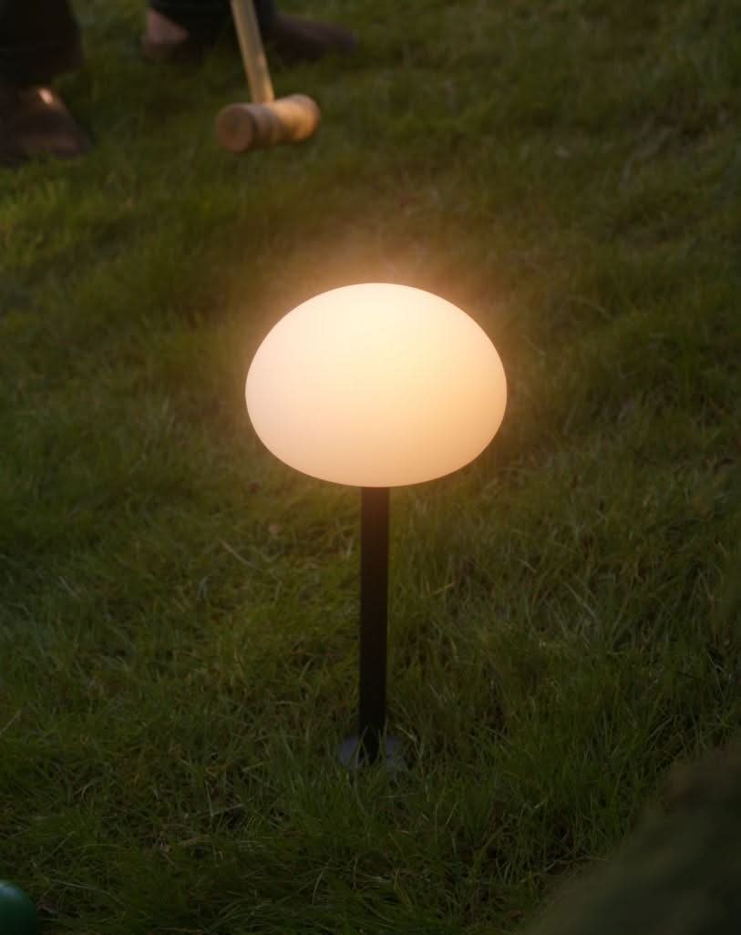 Lampe allumée posée dans l'herbe, lumière chaude et ambiance crépusculaire.
