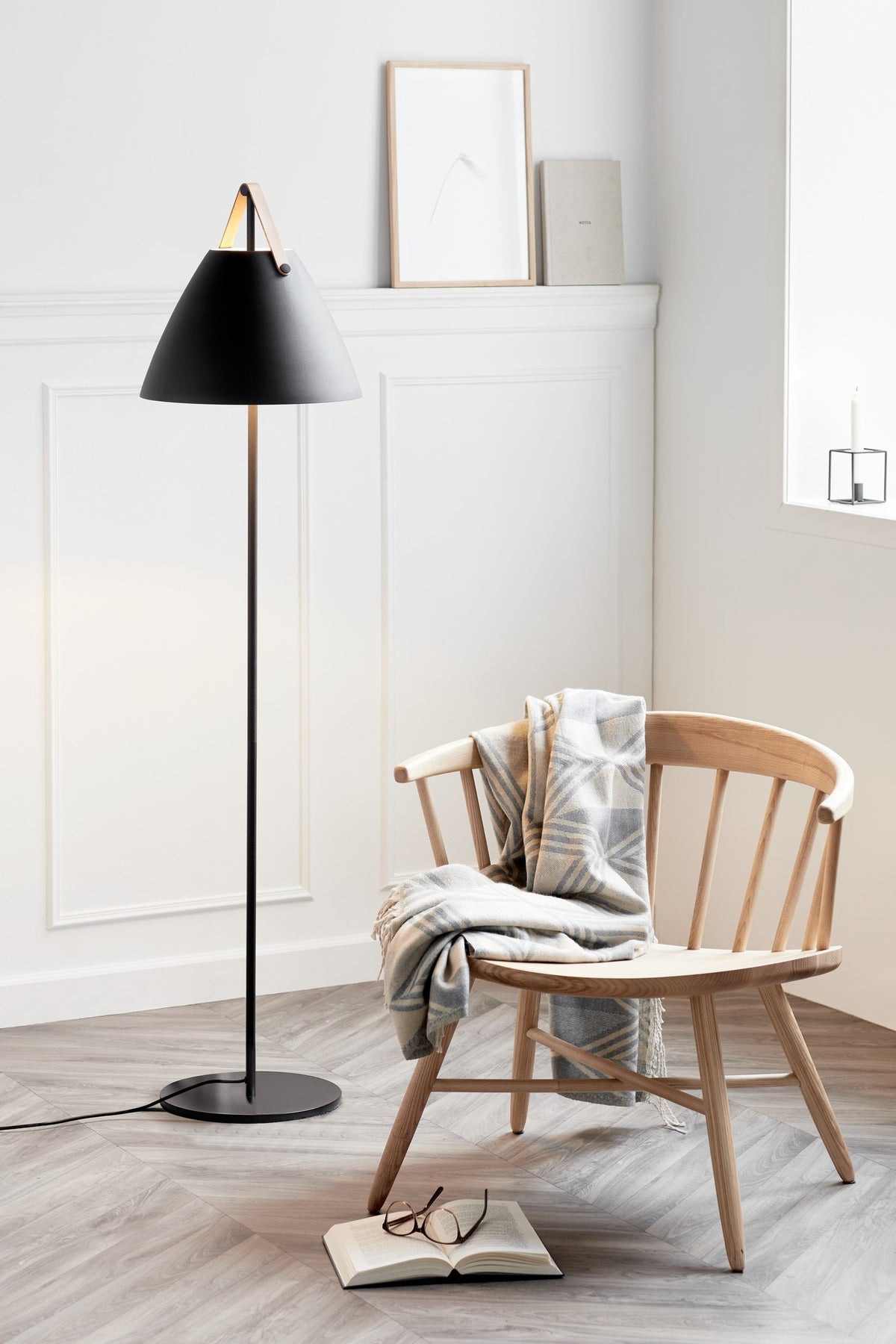 Mise en ambiance salon, lampadaire allumé à côté d'un fauteuil en bois.
