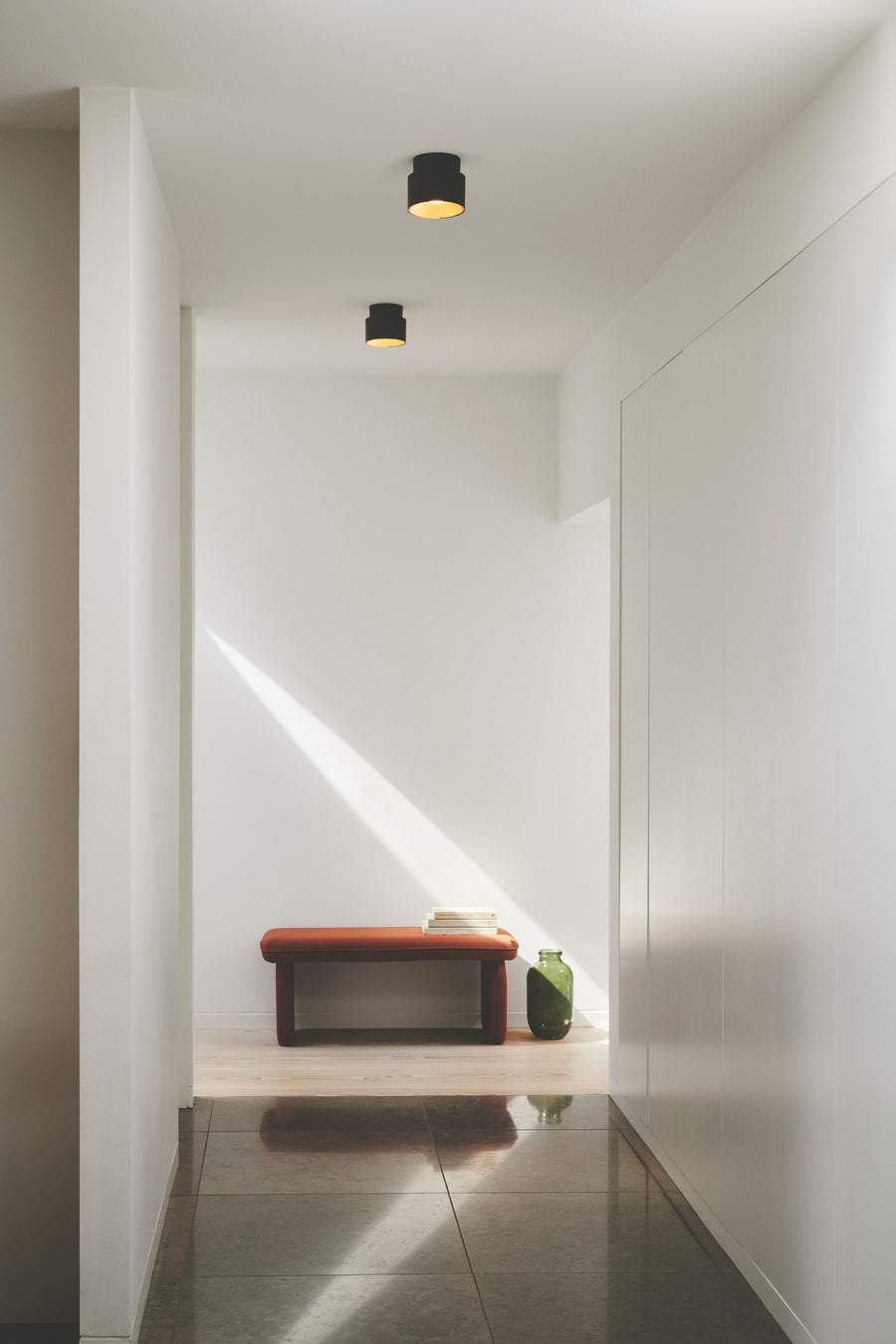Deux plafonniers noirs éclairant un couloir blanc minimaliste avec banc