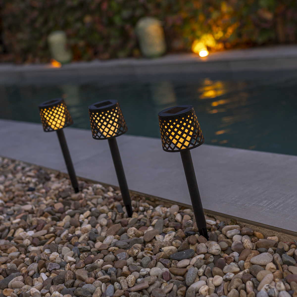 Trois balises solaires allumées diffusent une lumière chaude au bord de la piscine.