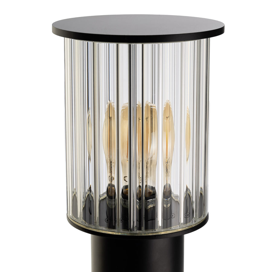 Gros plan sur le diffuseur cylindrique en verre strié et l'ampoule à filament visible.