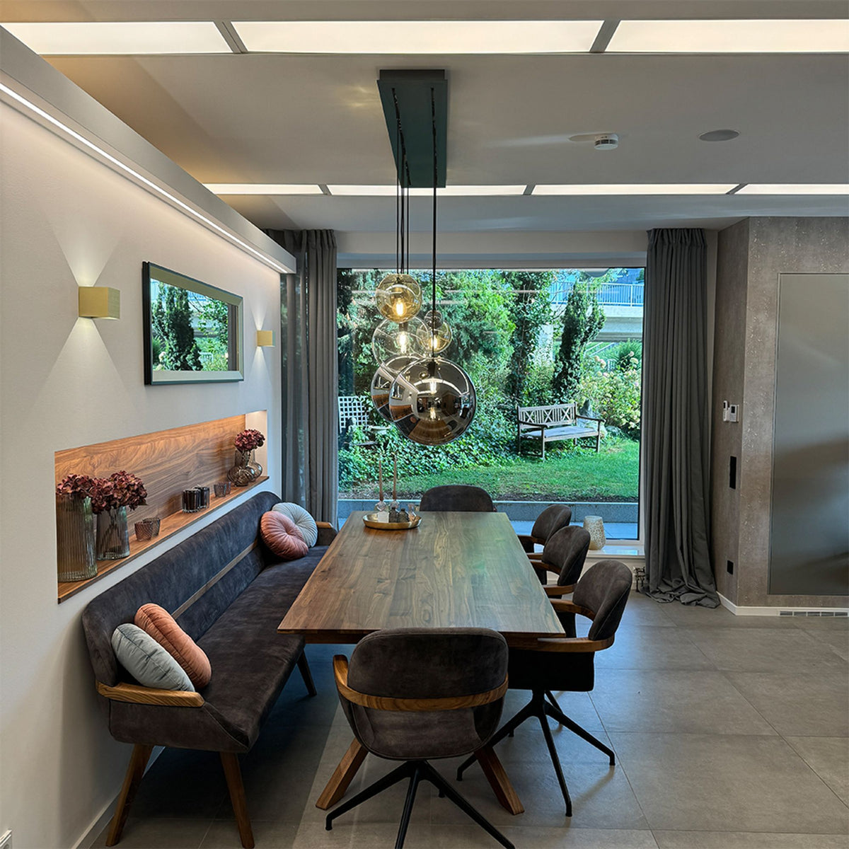 Suspension en verre miroir reflétant le jardin, au-dessus d'une table en bois massif.