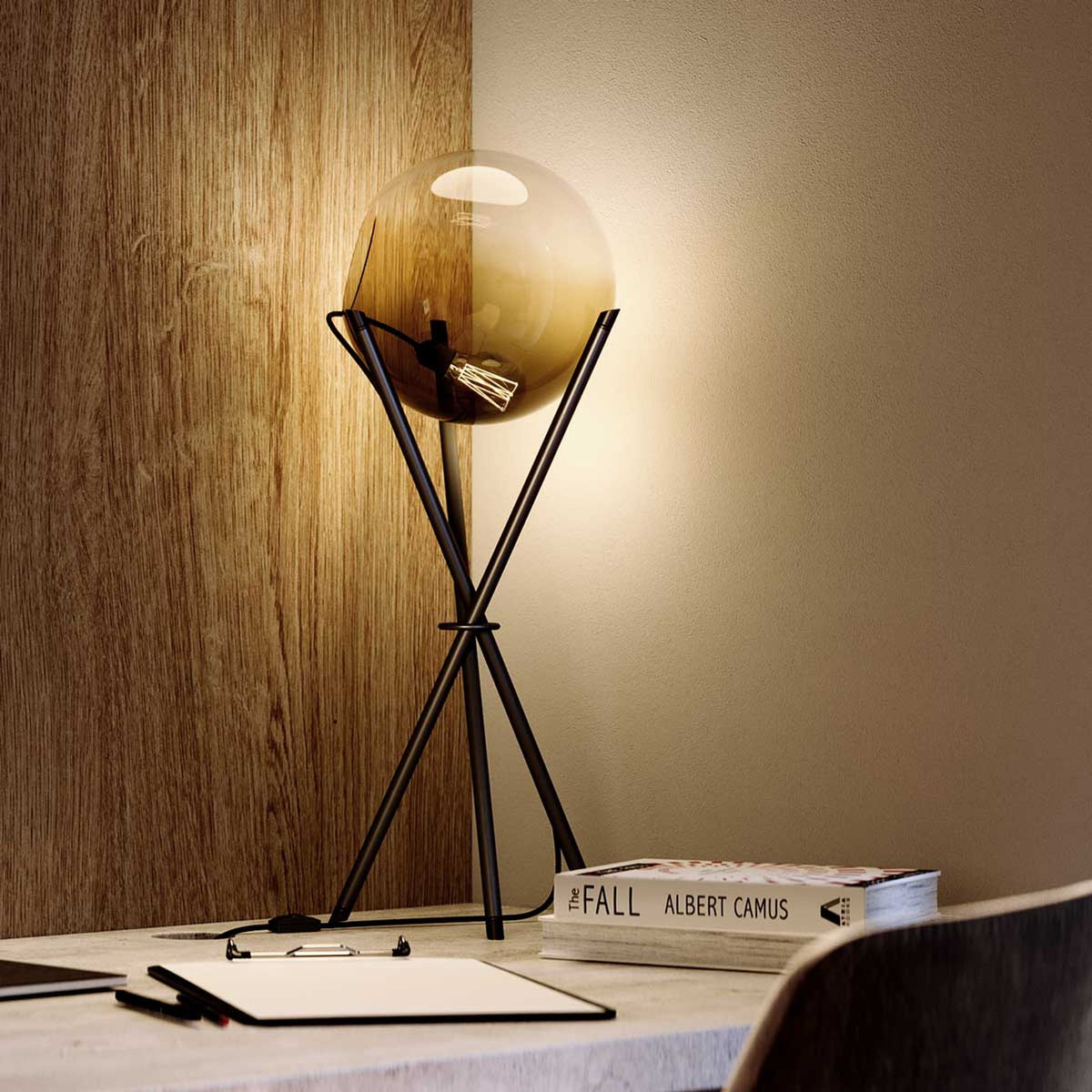 Lampe à poser noire avec globe en verre ambré allumé sur un bureau, ambiance chaleureuse
