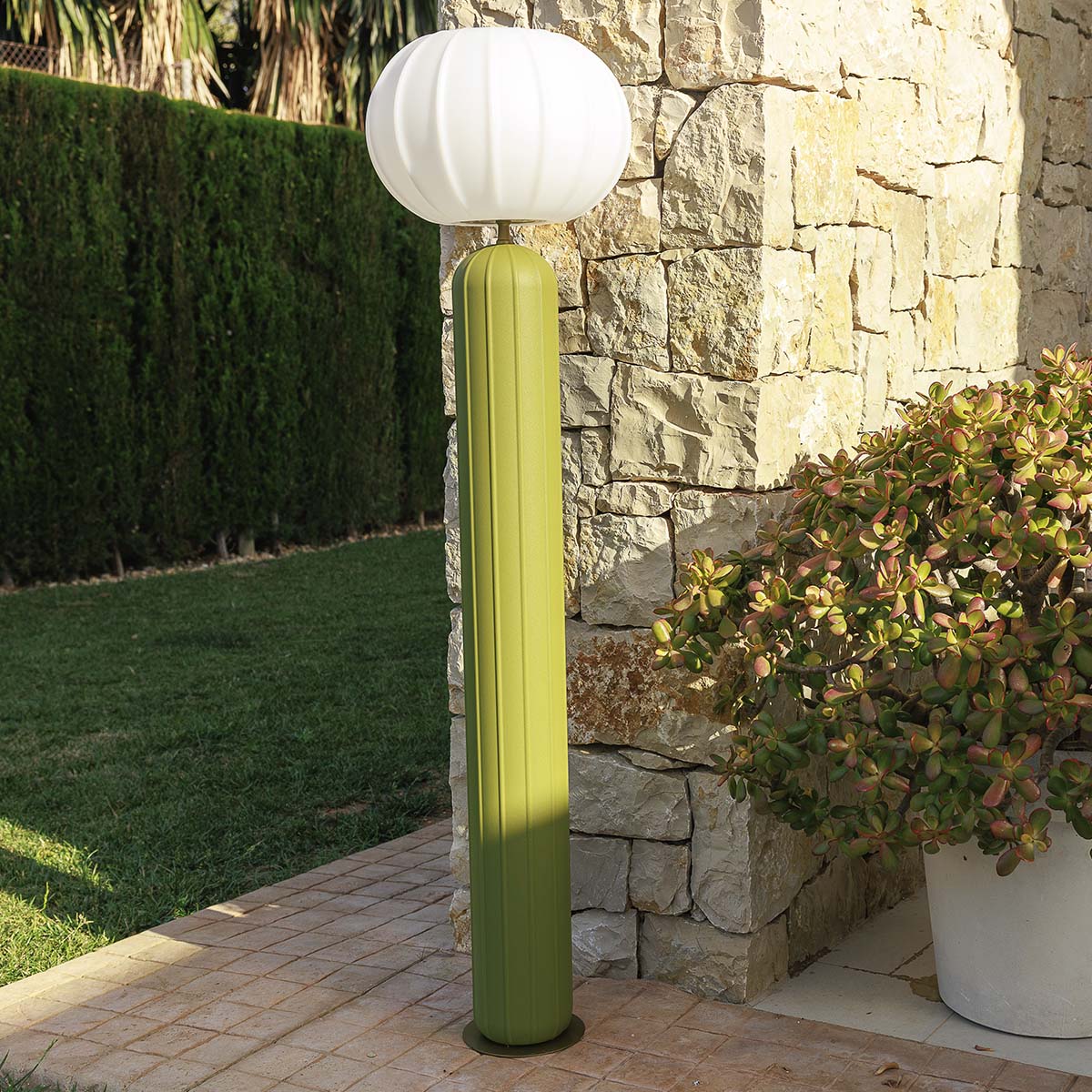 Détail du fût cannelé vert et du globe blanc contre un mur de pierre.