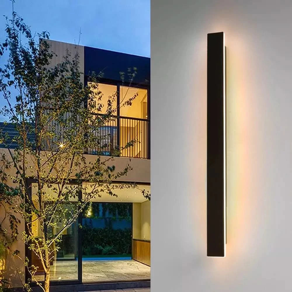 Luminaire mural noir vertical allumé au crépuscule devant une maison contemporaine et un arbre