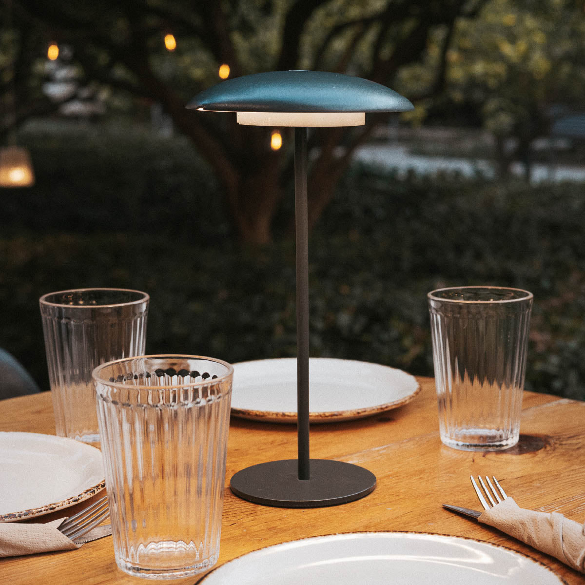 Lampe bleu-vert entourée de verres et assiettes sur une table en bois