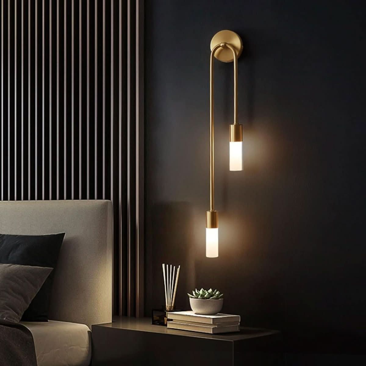 Chambre sombre, applique murale dorée éclairant une table de nuit et un livre.