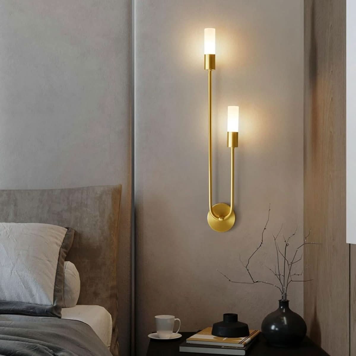 Mise en ambiance chambre : applique dorée allumée au-dessus d'une table de nuit.