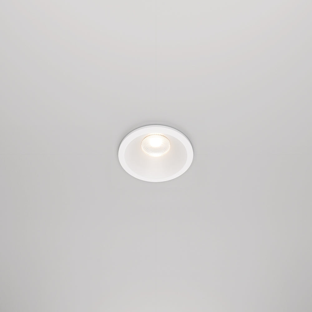 Spot encastré blanc vu de face dans un plafond, lumière allumée