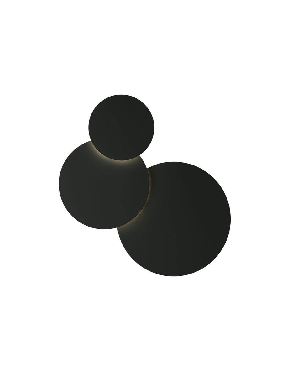 Vue de face du luminaire noir, trois cercles décalés laissant passer une lumière chaude.