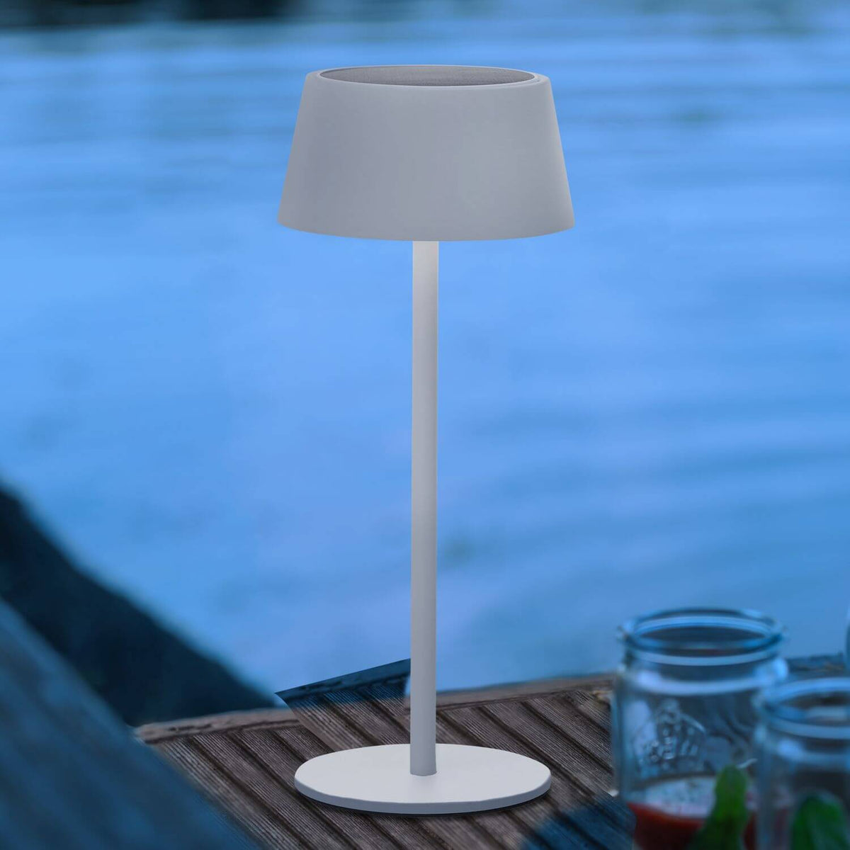 Mise en ambiance en bord de piscine au crépuscule, lampe blanche allumée sur table en bois