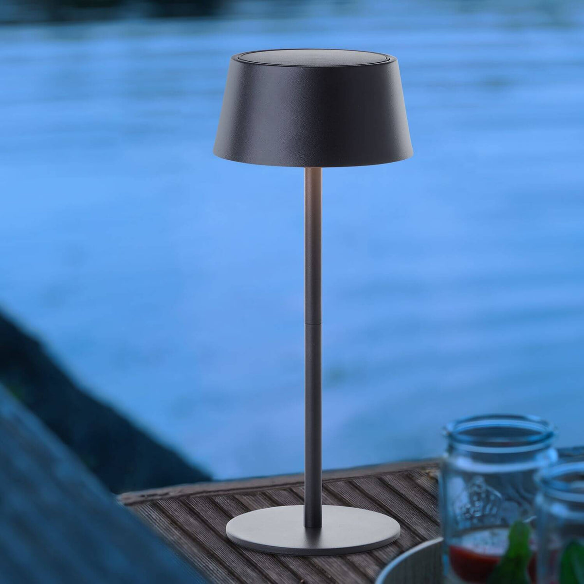 Lampe allumée posée sur une table en teck au bord d'une piscine.