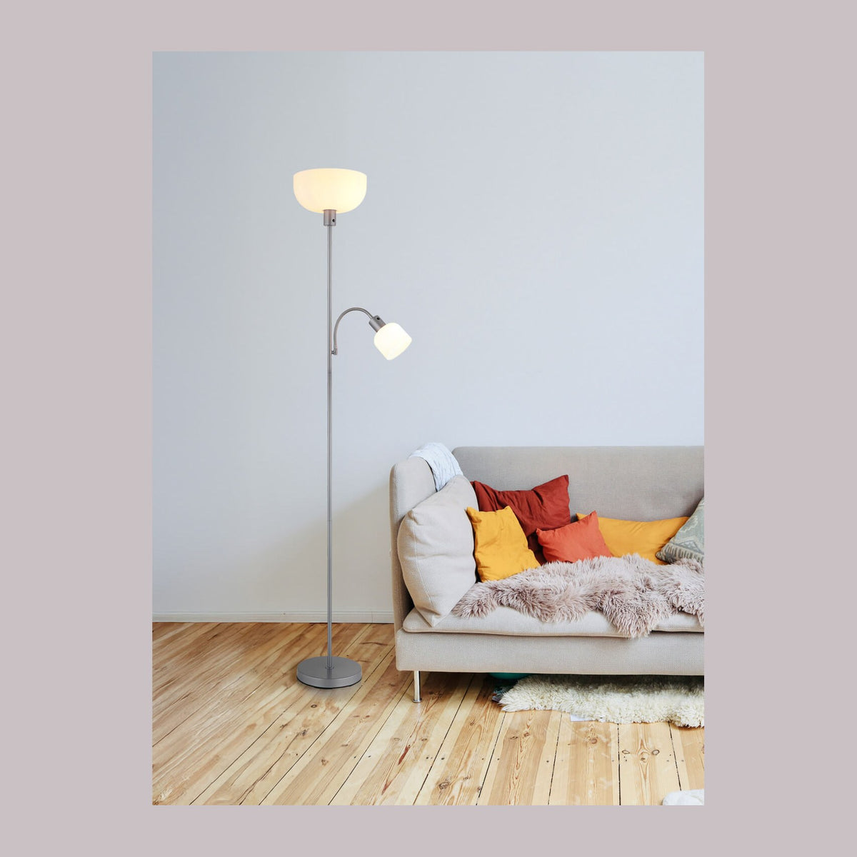 Lampadaire argenté allumé près d'un canapé beige avec coussins colorés.