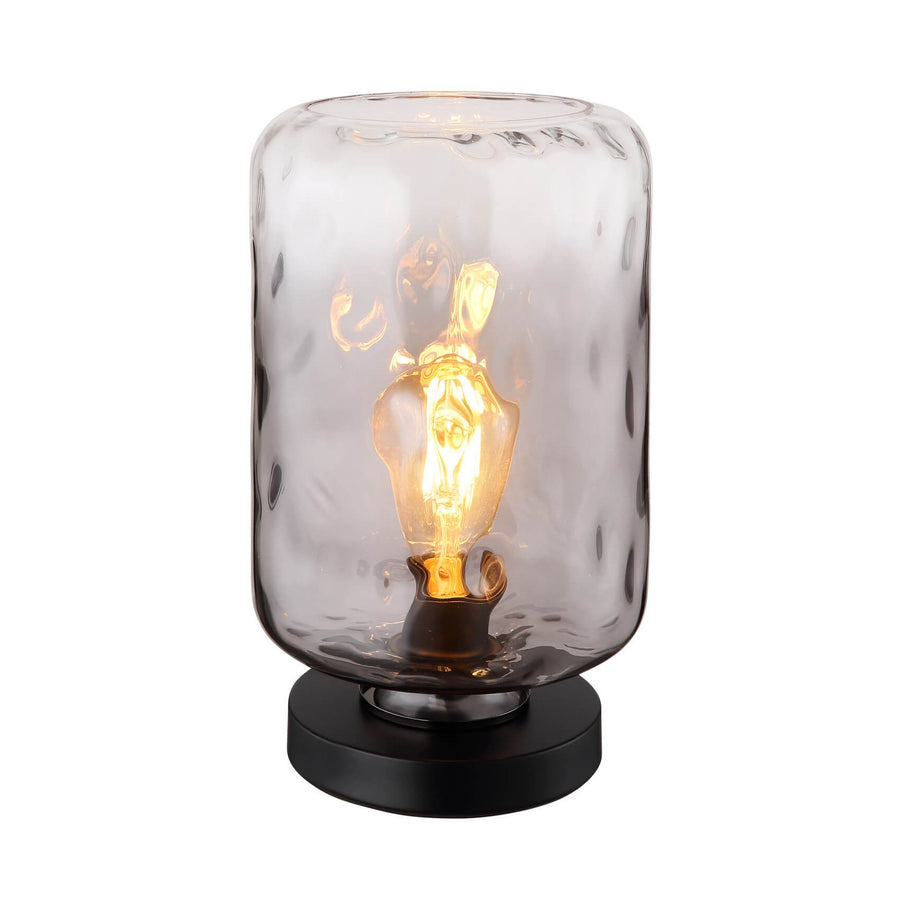 Lampe à poser noire avec abat-jour cylindrique en verre martelé, ampoule Edison allumée.