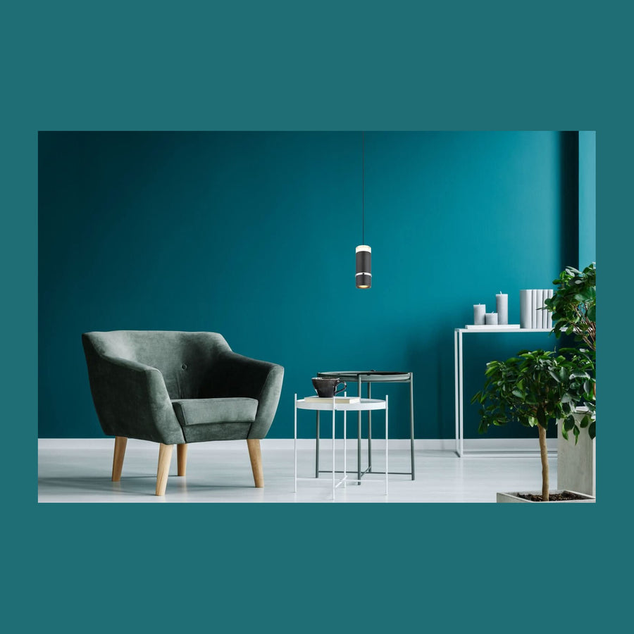 Suspension noire cylindrique suspendue dans un salon au mur bleu pétrole avec fauteuil et tables.