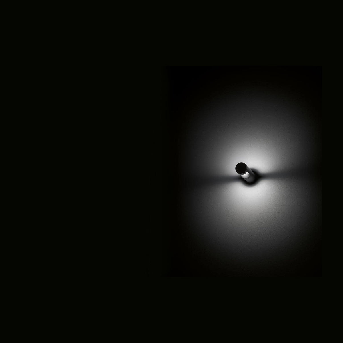 Luminaire cylindrique anthracite allumé dans le noir, halo lumineux projeté sur le mur