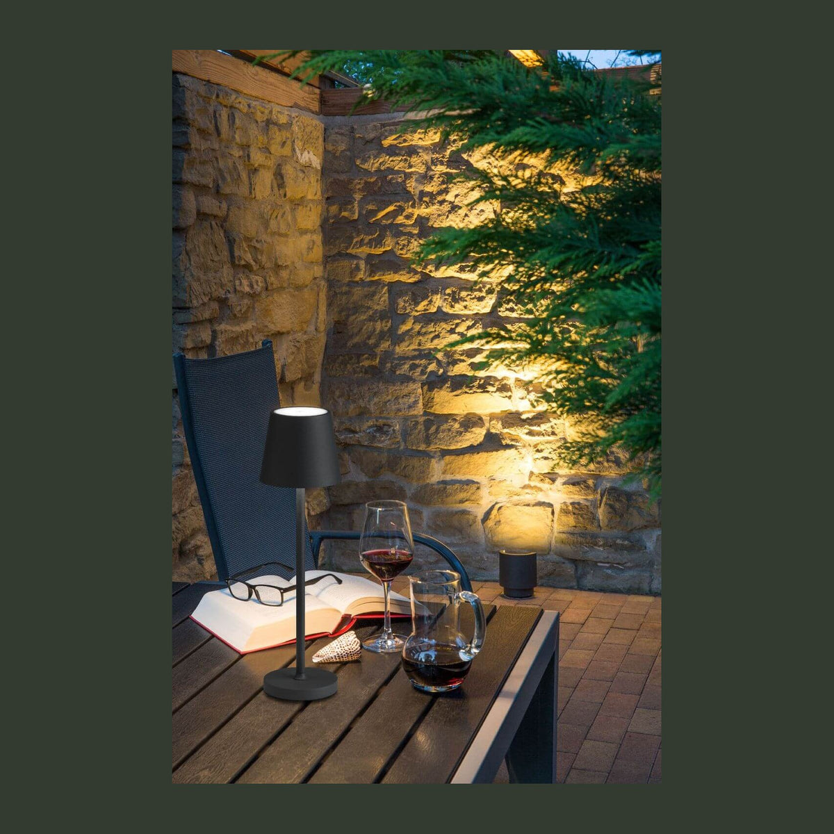Mise en ambiance nocturne d'une terrasse en pierre avec lampe de table et verre de vin