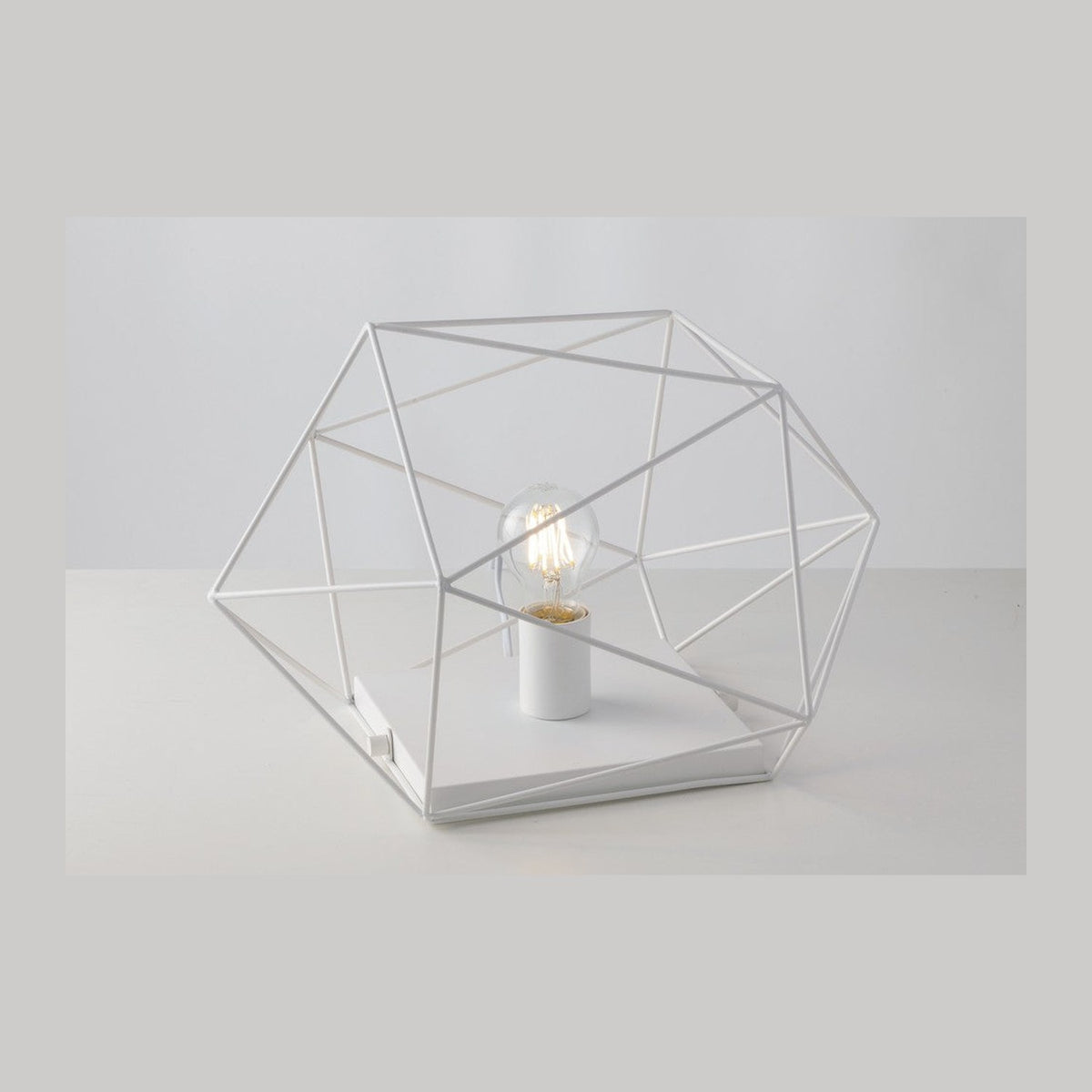 Lampe à poser blanche de face, structure géométrique en fil métallique autour d'une ampoule