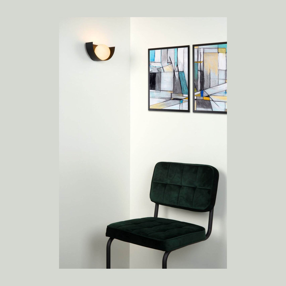 Applique murale noire allumée sur un mur blanc, au-dessus d'une chaise verte