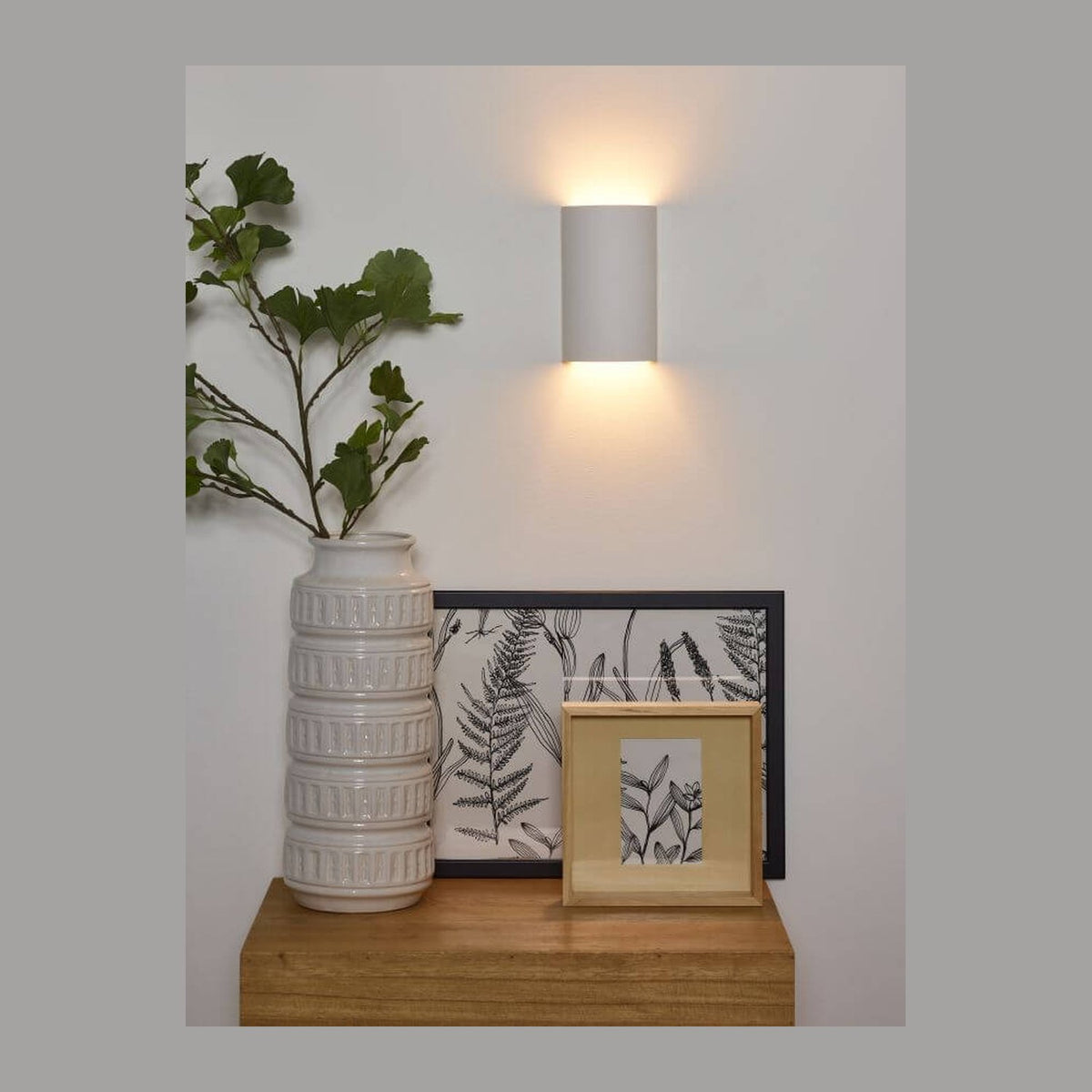 Applique murale blanche allumée sur un mur blanc avec vase et cadre