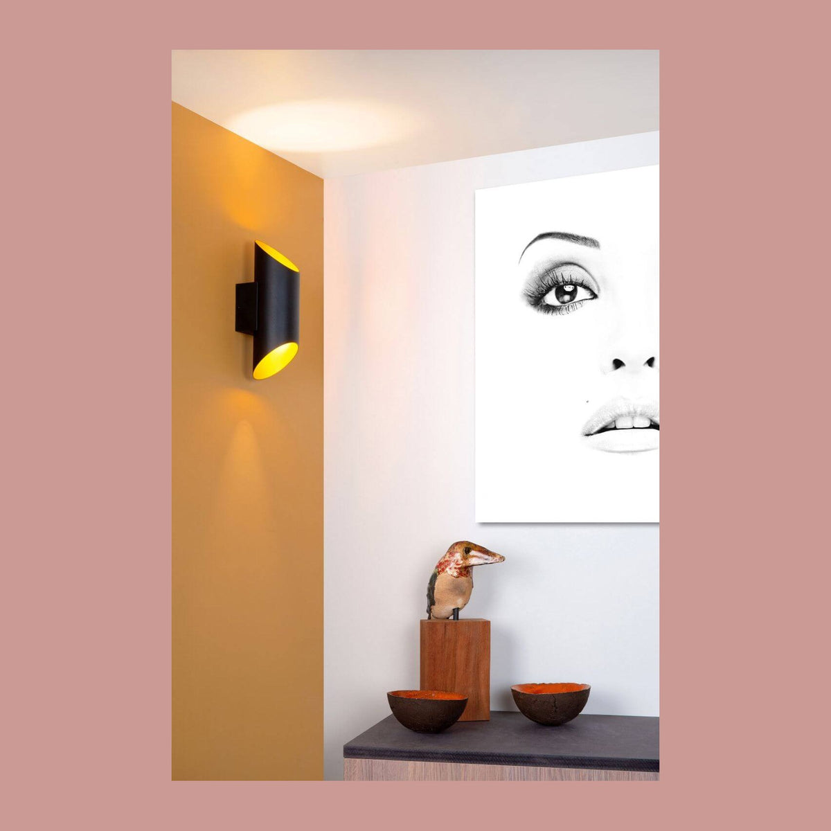 Applique cylindrique noire et dorée éclairant un mur ocre dans un intérieur contemporain