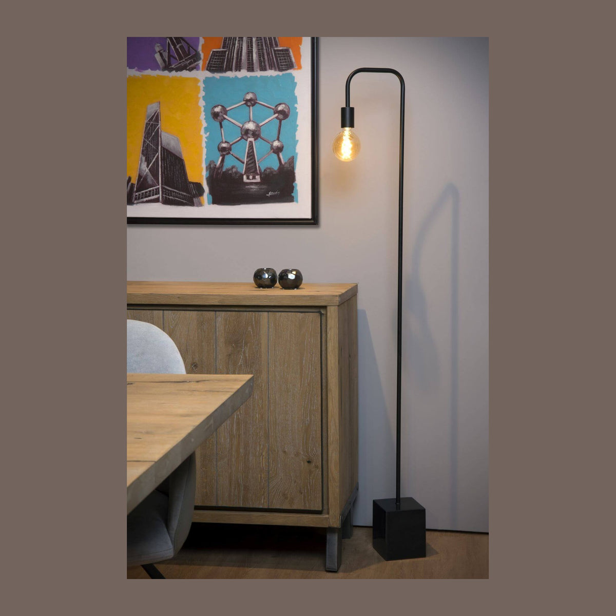 Lampadaire noir allumé dans un salon devant un buffet en bois et une toile encadrée