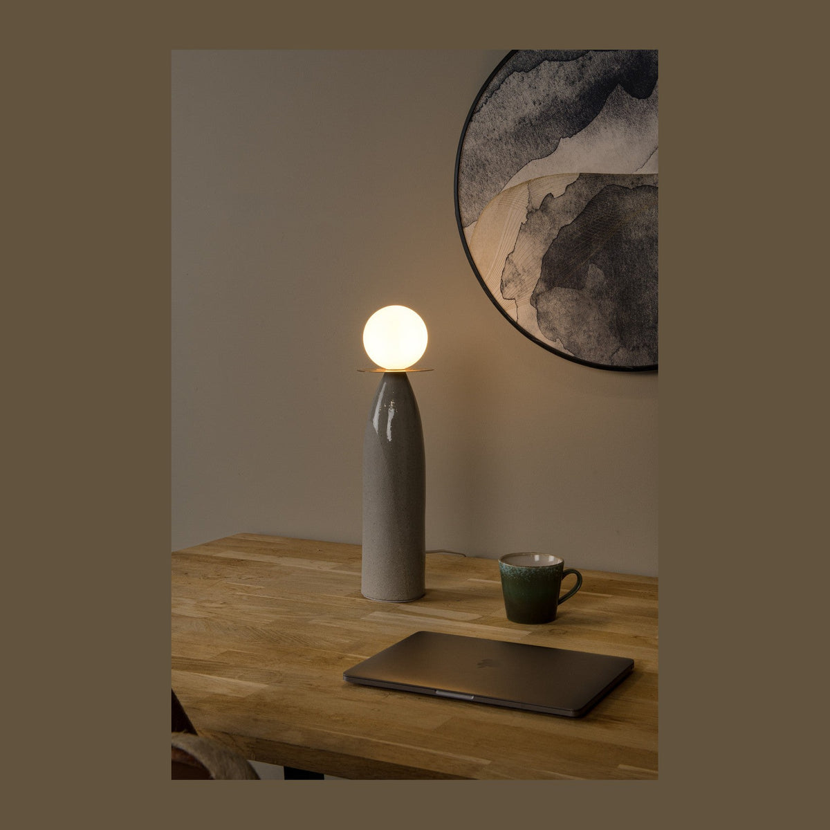Lampe posée sur table en bois, près d'un ordinateur et d'une tasse, ambiance chaleureuse
