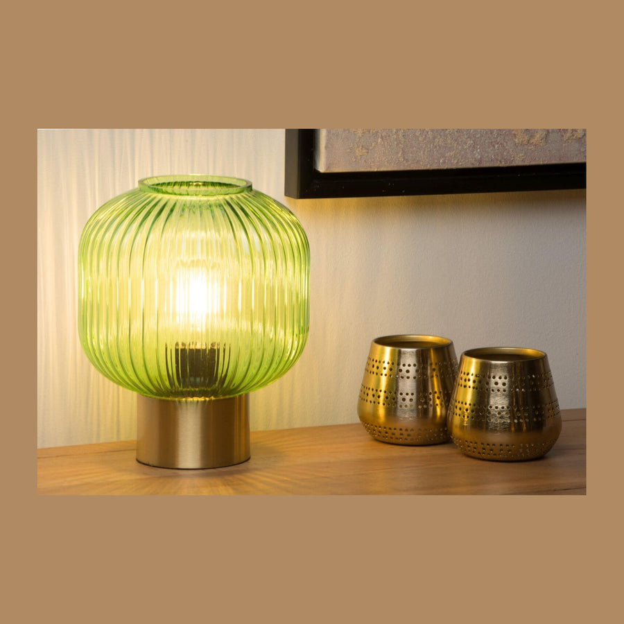 Lampe à poser allumée sur une table en bois, entourée de deux photophores dorés